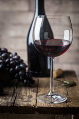 Red wine in a glass and ripe grapes on wooden table