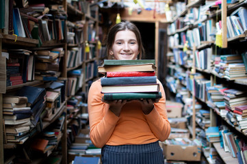 girl student holds a stack of books in the library, she searches for literature and offers to read,...