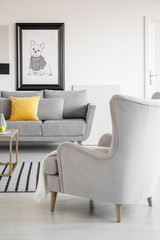 Comfortable wing back armchair in elegant living room interior with sad dog poster in black frame