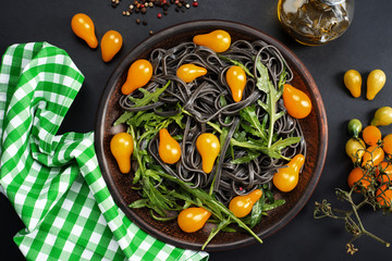 Black pasta with bright juicy yellow cherry tomatoes in the form of light bulbs and arugula on a dark background. Delicious smart food