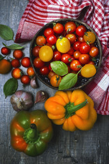 Farm harvest. Multi-colored cherry tomatoes and bright juicy peppers on a gray wooden board. Author retouch