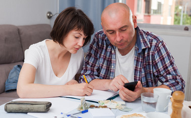 Mature couple with phone calculation money sitting at table