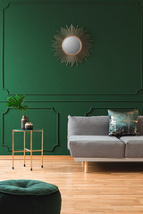 Golden sun shape like mirror on green wall of living room interior with scandinavian sofa with pillows © Photographee.eu