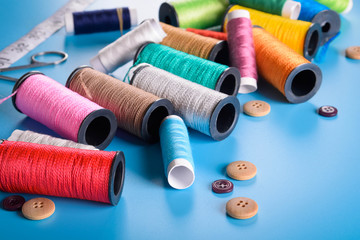 Sewing kit: scissors, measuring tape, thimbles, threads and buttons. Composition with threads and sewing accessories on blue background