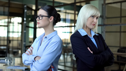 Two business women standing back to back looking angrily, career competition