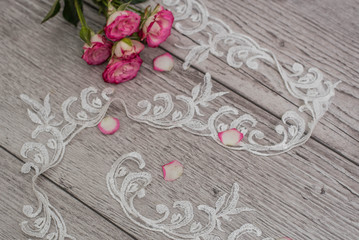 White wooden background with white spring flowers roses and lace ribbon. Happy womans day. The texture of lace on wooden background.