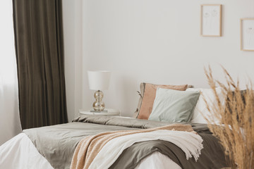 White and beige blankets on grey duvet on comfortable bed in bright bedroom interior