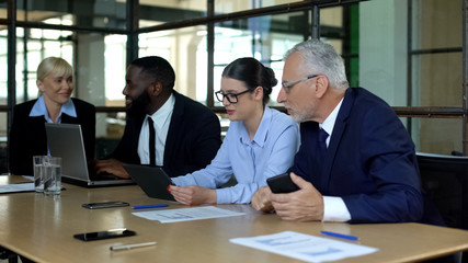 Company colleagues discussing news in office, using modern gadgets, teamwork