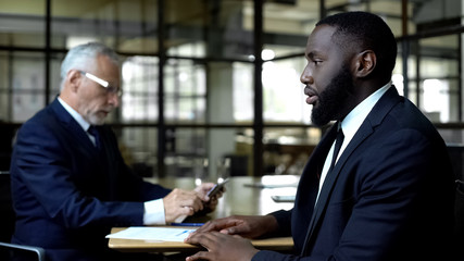 Nervous afro-american man at job interview, strict boss looking through resume