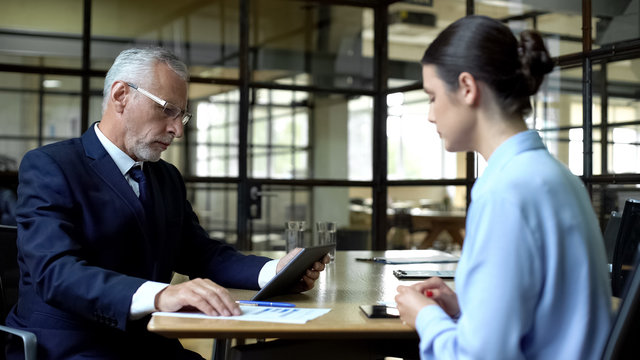 Aged businessman scrolling company app on tablet unhappy with work results