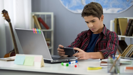Lazy kid enthusiastically playing smartphone game instead homework, discipline