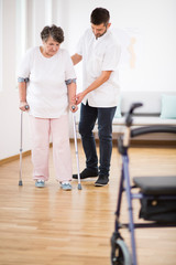 Senior woman at hospital learning how to walk on crunches and supporting male nurse