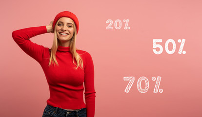 Blonde girl smiles with red hat and cardigan. Pink background for blank space for your discount text
