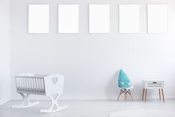 Mockup of empty posters on white wall in baby's bedroom interior with cradle and blue pillow. Real...