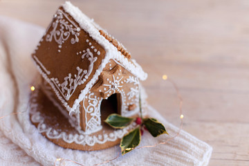 Gingerbread house, Christmas cozy decorations on wooden and knitted background with glares....