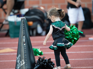 Cute little girl dressed in a cheerleader costume at a football game