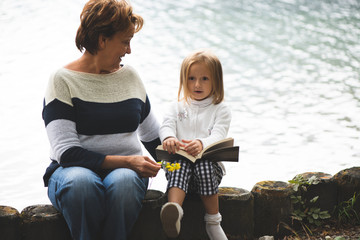 grandmother and granddaughter read a book and dream on the lake