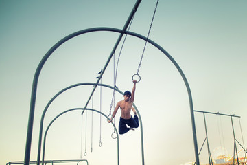 Fototapeta na wymiar A young man athlete working out on traveling rings on muscle beach, Santa Monica, California