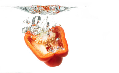 Sliced in half red bell pepper falls to the water, causing bubbles and scattered water.