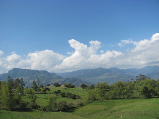 Fototapeta na wymiar Paisaje verde de montañas y una casa en cercanía en la colina