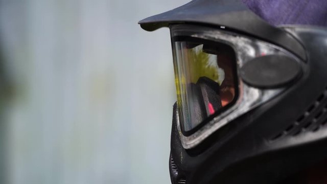 Man in paintball mask is being hit with yellow ball. Slow motion.