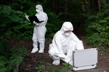 Ecological problem. Pollution. Examine soil. Scientist working in forest in protective mask and suit taking water and soil samples. Chemist makes an analysis of the environment for radiation. 
