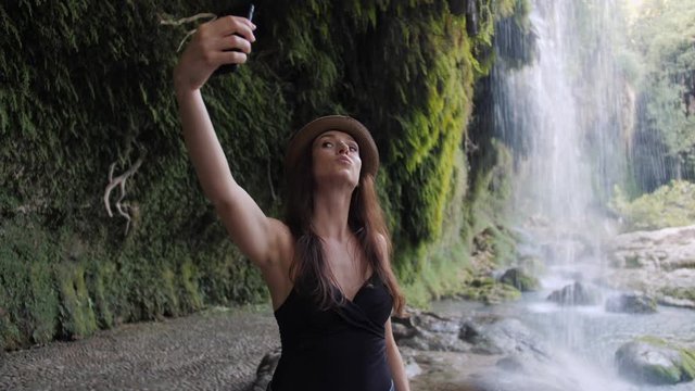 Woman taking selfie using phone near waterfall at national park happy smiling enjoying nature and lifestyle on vacation.