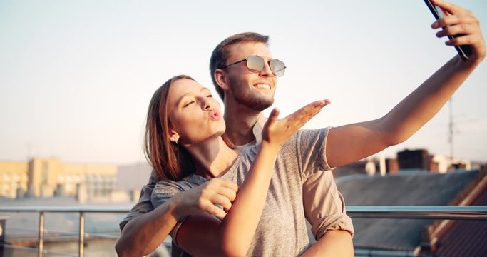 Joyful loving couple hugging, smiling and making selfie on smartphone at summer sunset, sweetness