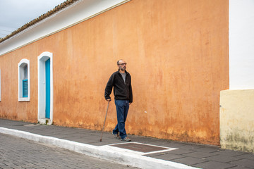 Disabled man walks with walking stick and difficulty on the street