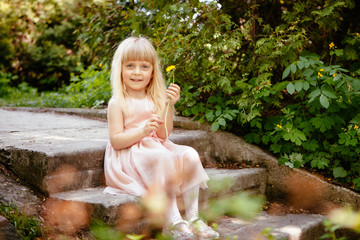 Beautiful little girl sitting and smiling with dandelion flower in hand