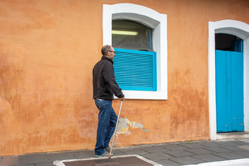 Disabled man walks with walking stick and difficulty on the street