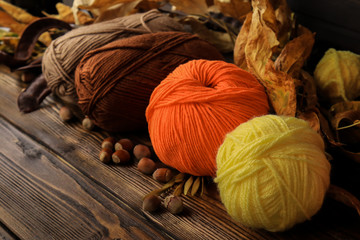 Composition with yarn balls and autumn leaves on wooden background