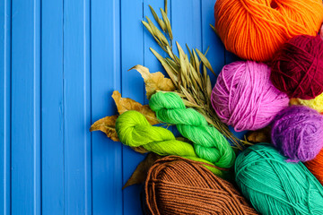Composition with yarn balls and autumn leaves on color wooden background