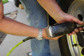 The hands of a man holding an impact gun as he reinstalls the front wheel of a vehicle