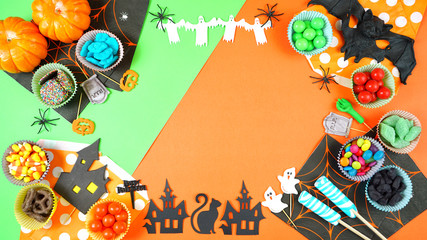 Fototapeta na wymiar Halloween candy and paper symbols on bright modern orange and green background with copy space.