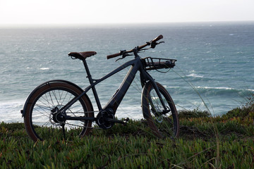 Fototapeta na wymiar classic style electro powered bicycle with front rack at the coast with ocean in the background