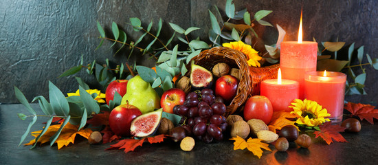 Happy Thanksgiving cornucopia table setting centerpiece decorated with autumn leaves, fruit, nuts and orange burning candles, web banner. - obrazy, fototapety, plakaty