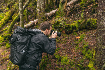 Nature still photography photographer man with professional slr camera taking picture of wild mushroom in forest during trail hike.