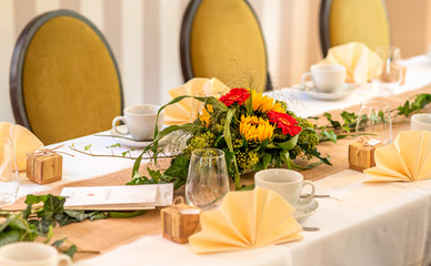 Festive table setting. Coffee cups, glasses, bouquets of sunflowers and red gerberas, on a white tablecloth.
