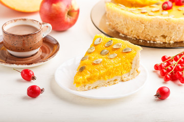 Traditional american sweet pumpkin pie decorated with hawthorn red berries and pumpkin seeds with cup of coffee on a white wooden background. side view, selective focus.