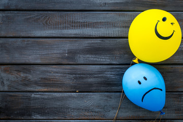 Treat depression concept. Balloons with sad and smiling faces on dark wooden background top view copy space