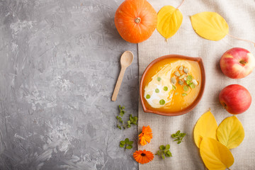 Traditional pumpkin cream soup with seeds in clay bowl on a gray concrete background with linen textile. top view