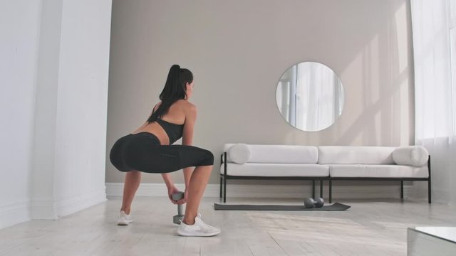 Young fitness woman doing squat with dumbbells in hands
