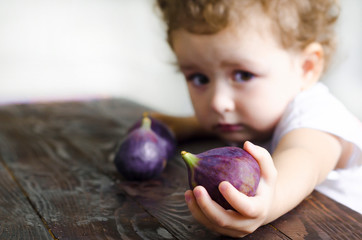 Fototapeta premium little girl holds ripe figs berries in her hands. the child looks at the camera and holds out the fruit. soft focus, blur