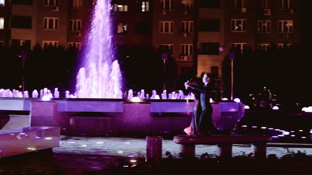 A boy and a girl dance around a bright fountain at night. very spectacular. Slow playback.