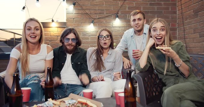 Happy friends watching sports game on tv, cheering for favorite team and making win gesture