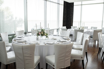 Wedding table setting decorated with fresh flowers. White plates, silverware, white tablecloth and white room. Wedding floristry. Banquet table for guests. Bouquet with roses, hydrangea and eustoma