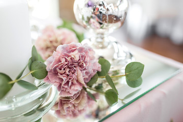 The wedding table setting for the newlyweds is decorated with fresh flowers of carnation, rose, anthurium and eucalyptus leaves. Silver candlesticks, white candles. Wedding floristry. Closeup details