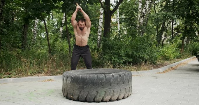 Muscle athlete strongman man hits a hammer on a huge wheel. Slow motion