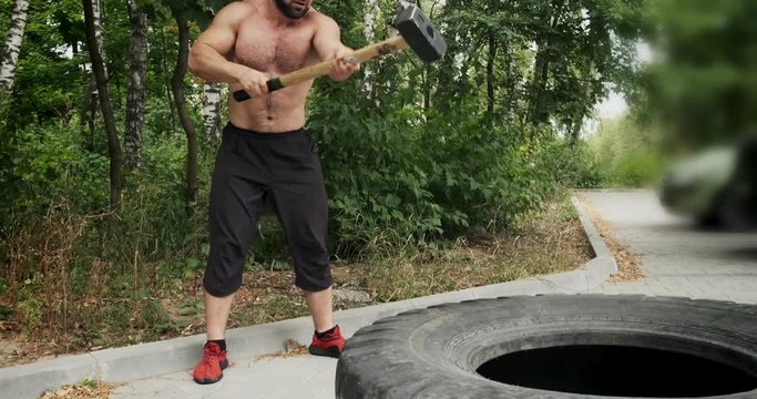 Muscle athlete strongman man hits a hammer on a huge wheel. Slow motion